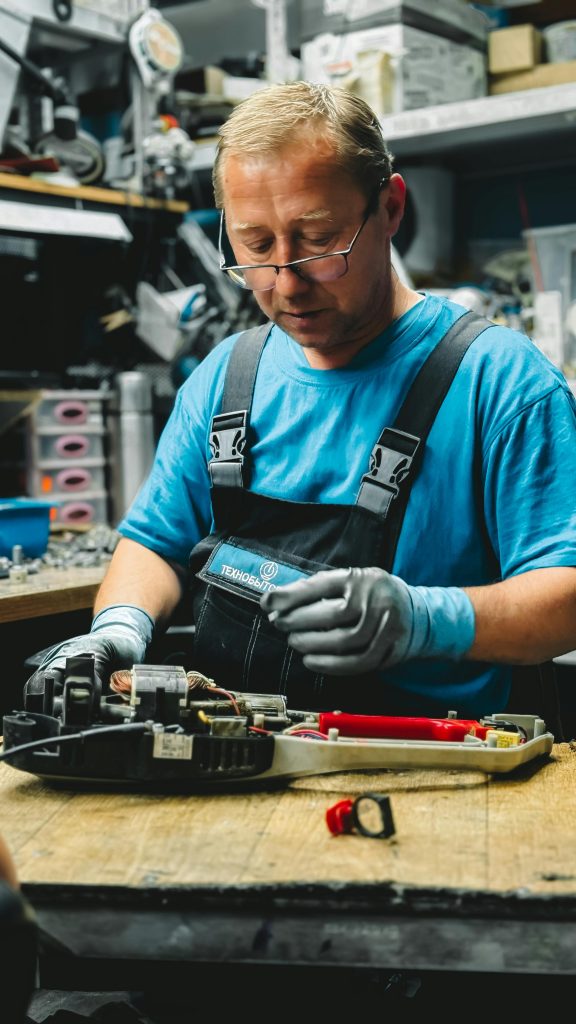 Skilled mechanic working on mechanical device in cluttered workshop setting.